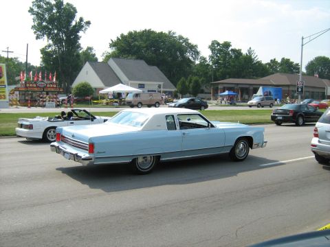 1988 Mercury Grand Marquis - A classic Lincoln Continental cruises by a roadside event with other vehicles present.