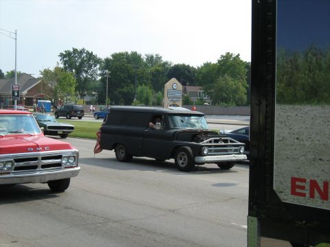 1988 Mercury Grand Marquis - Black panel van driving on a street, hood open, with a red GMC pickup truck nearby.
