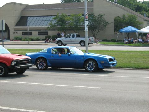 1988 Mercury Grand Marquis - A blue 1977 Pontiac Firebird Trans Am drives down the road next to a red pickup truck.