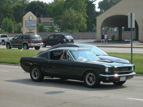 1988 Mercury Grand Marquis - A 1965 Ford Mustang Fastback is seen on the road with other cars and buildings.