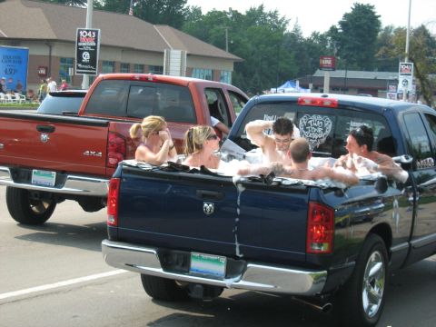 1988 Mercury Grand Marquis - People ride in hot tubs installed in the beds of pickup trucks during a parade.