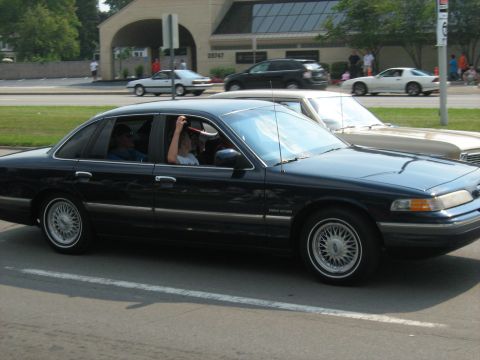 1988 Mercury Grand Marquis - A dark sedan drives down the road with passengers inside.