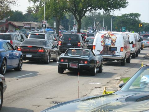 1988 Mercury Grand Marquis - A line of vehicles on a street, including a black Corvette Stingray and a van with a graphic on its side.