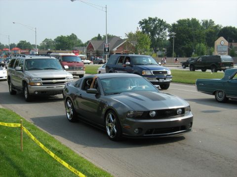 1988 Mercury Grand Marquis - A line of vehicles, including a gray Ford Mustang, drives down a street on a sunny day.