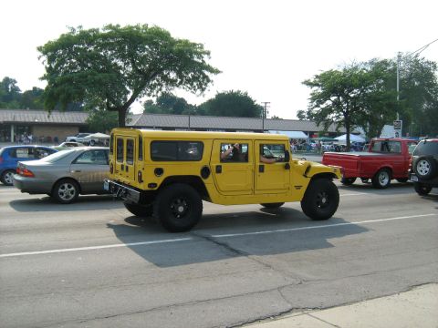 1988 Mercury Grand Marquis - A yellow Hummer H1 is seen driving on a road with other vehicles and buildings in the background.