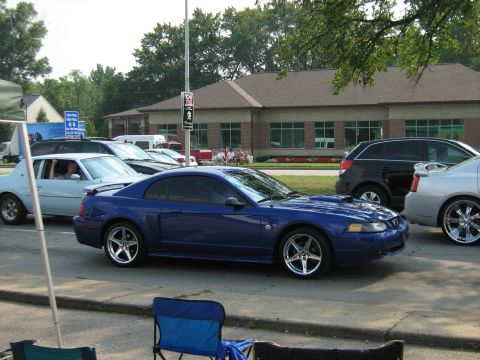 1988 Mercury Grand Marquis - A blue Ford Mustang is parked on the street, with other vehicles and a building in the background.