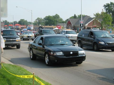 1988 Mercury Grand Marquis - A black sedan is seen driving in a procession of vehicles on a sunny day.