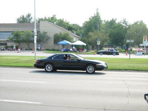 1988 Mercury Grand Marquis - A black coupe drives down the road with a police car in the background.