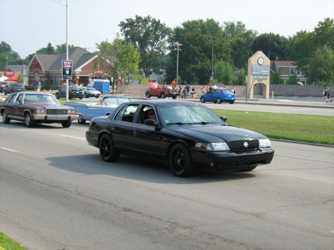 1988 Mercury Grand Marquis - A black sedan drives down the road, with other vehicles and buildings in the background.