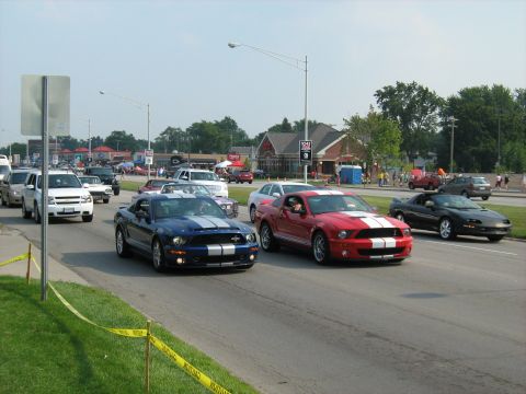 1988 Mercury Grand Marquis - Two Ford Mustangs, one blue and one red, are seen driving in a procession with other vehicles.
