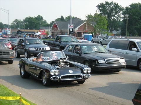 1988 Mercury Grand Marquis - A classic black convertible cruises down the road with its hood open, revealing the engine.