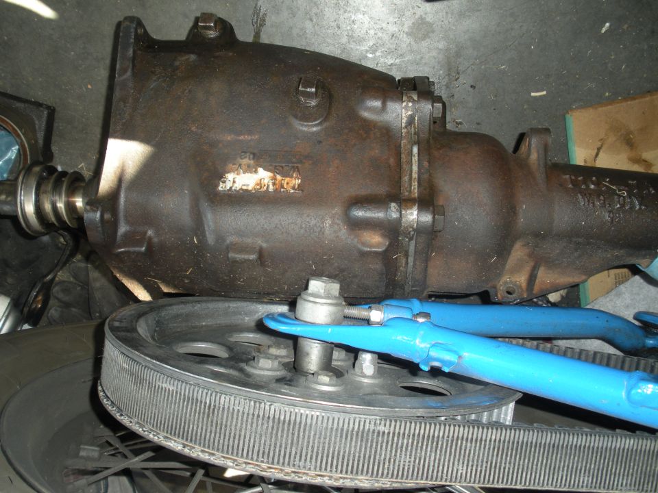 Rusty cast iron automatic transmission on a shop floor with air filter and blue links