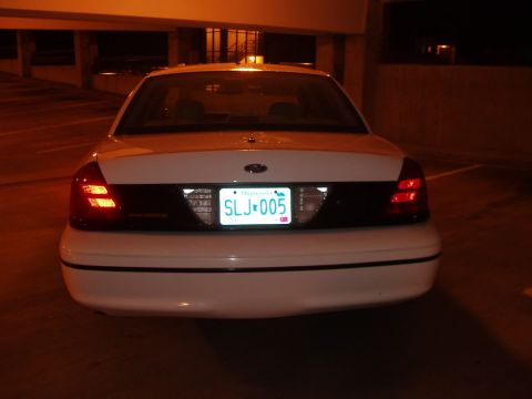2003 Ford Crown Victoria - The rear of a white Ford Crown Victoria is shown at night, with its license plate illuminated.