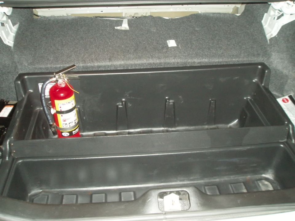 Sedan trunk with black plastic organizer tray and red fire extinguisher