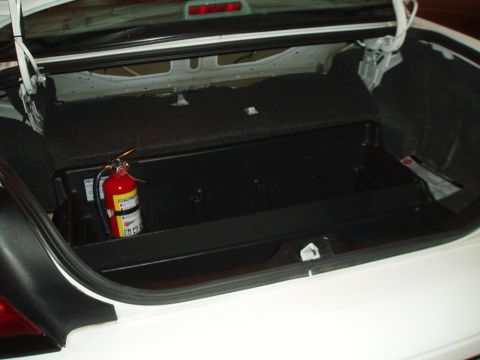 2003 Ford Crown Victoria - The open trunk of a vehicle is shown, with a single red bottle visible inside the cargo area.
