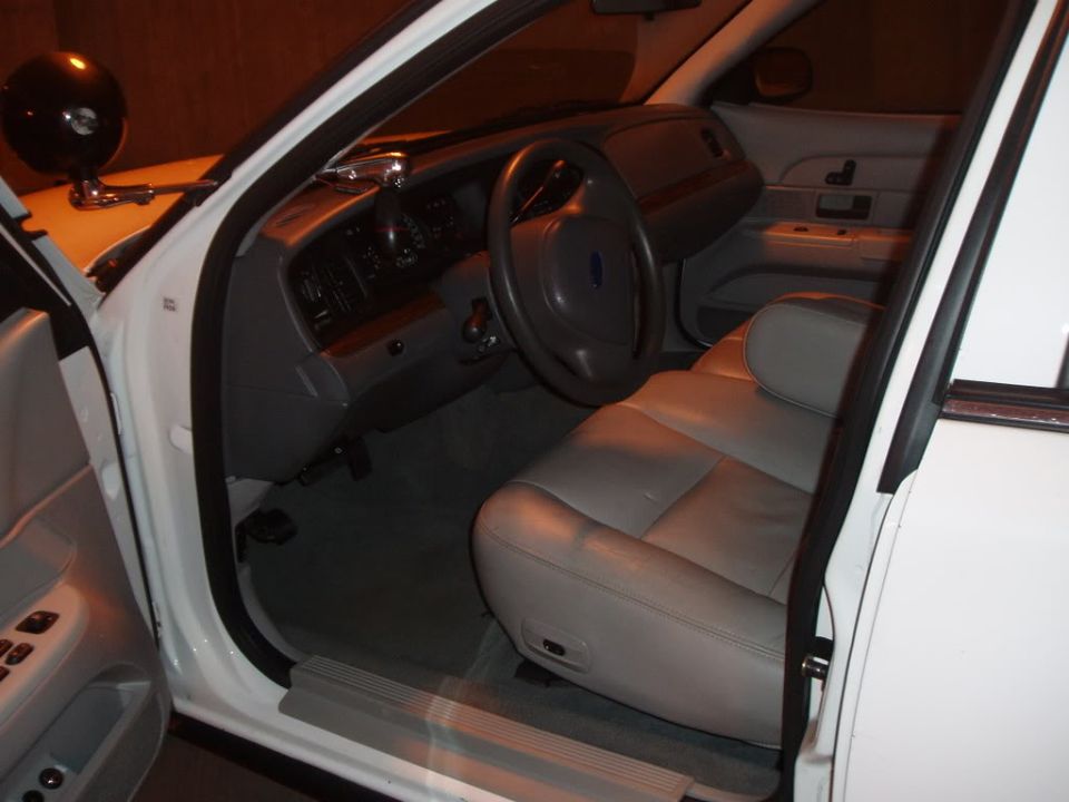 Open driver's door of white Ford sedan showing gray leather seat and pillar spotlight