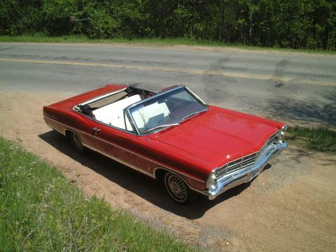 1967 Ford Galaxie - Red 1967 Ford Galaxie convertible with white interior parked on a dirt road beside a highway.