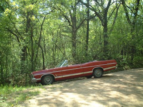 1967 Ford Galaxie - A red 1967 Ford Galaxie convertible is parked on the side of a dirt road, surrounded by trees.