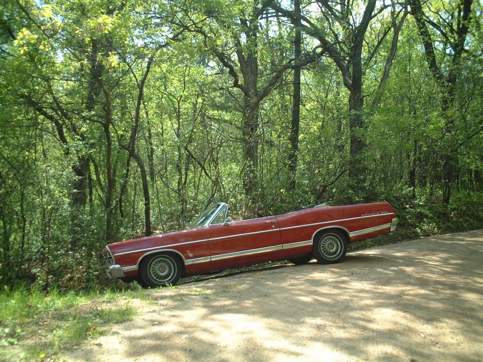 Red 1967 Ford Galaxie 500 convertible parked in profile on a wooded dirt road