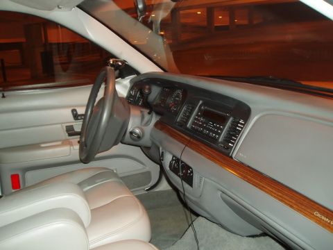 2003 Ford Crown Victoria - The interior of a 2003 Ford Crown Victoria features wood grain trim accents and light-colored leather seats.