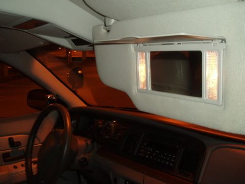 2003 Ford Crown Victoria - The illuminated vanity mirror on the sun visor is open, revealing the mirror and lights within the car's interior.