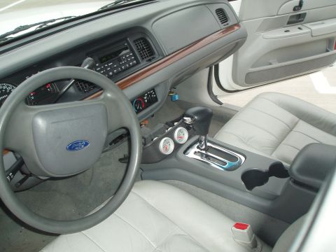 2003 Ford Crown Victoria - The interior of a 2003 Ford Crown Victoria features a dashboard, steering wheel, and light gray leather seats.