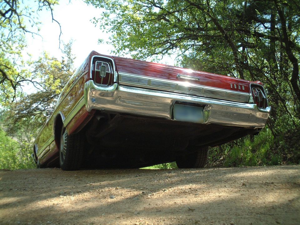 Low-angle rear view of red vintage Ford sedan on dirt road