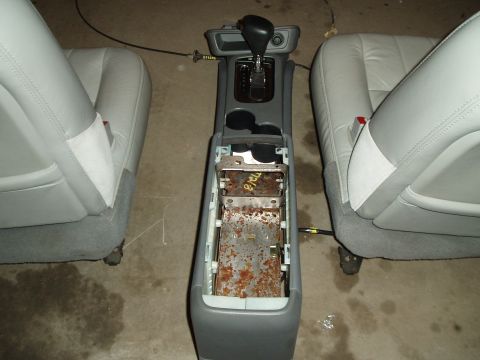 2003 Ford Crown Victoria - The center console of a vehicle has been disassembled, revealing rusty internal metal parts and the surrounding seats.
