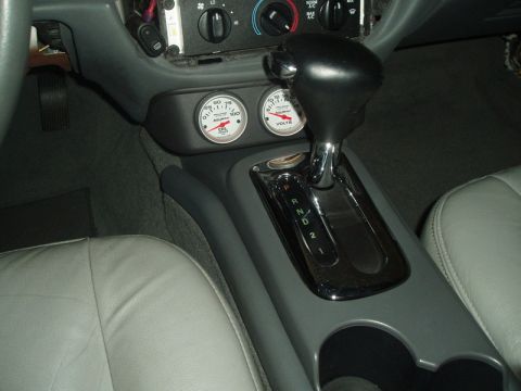 2003 Ford Crown Victoria - Interior center console of a vehicle showing a black leather automatic shifter with P-R-N-D-2-1 gate, flanked by gray leather seats and two…