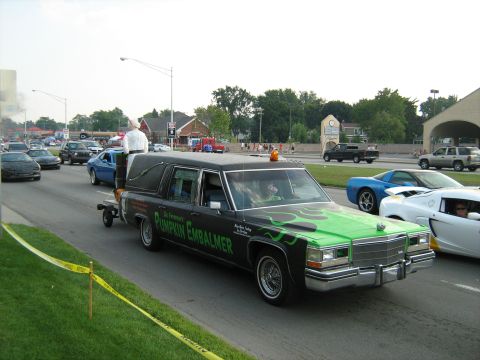 1988 Mercury Grand Marquis - Customized hearse with flame graphics and text, participating in a cruise event with other vehicles.