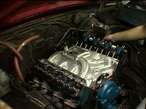 1967 Ford Galaxie - Close-up view of a car's engine bay, showing various mechanical parts and a hand working on the engine.
