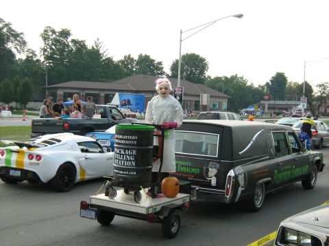 1988 Mercury Grand Marquis - A hearse, decorated with a creepy doll and Halloween theme, is part of a parade or event.