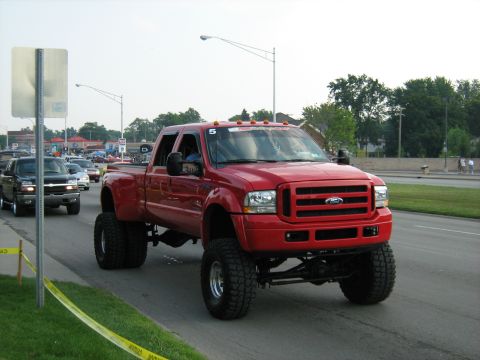 1988 Mercury Grand Marquis - A lifted red Ford F-350 Super Duty truck cruises down the road, with other vehicles visible in the background.