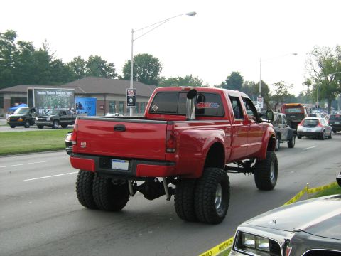 1988 Mercury Grand Marquis - Modified red dually pickup truck with custom exhaust and tires seen on the road.