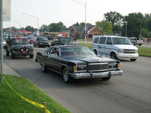 1988 Mercury Grand Marquis - A classic black Mercury Grand Marquis cruises down the road, part of a larger vehicle gathering.