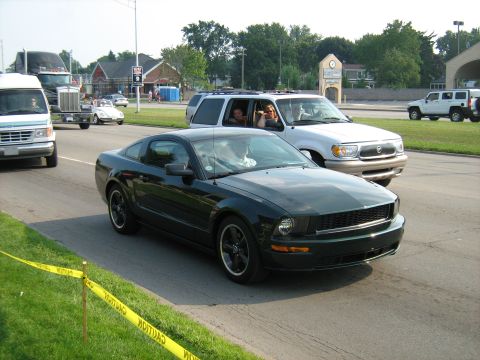 1988 Mercury Grand Marquis - A dark green coupe drives down the road, passing other vehicles and a caution tape barrier.