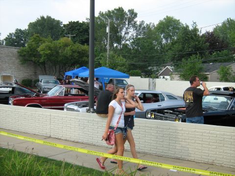 1988 Mercury Grand Marquis - Several cars are on display at an outdoor event, with attendees walking past.