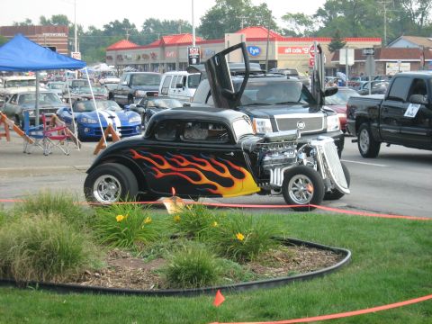 1988 Mercury Grand Marquis - A custom hot rod with flame decals is parked next to other vehicles, including a black SUV with its doors open.