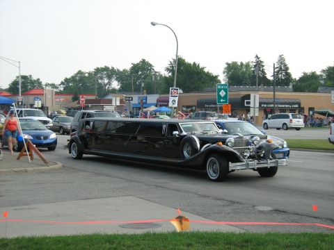 1988 Mercury Grand Marquis - A long black limousine is seen driving down a street, with other vehicles and buildings in the background.