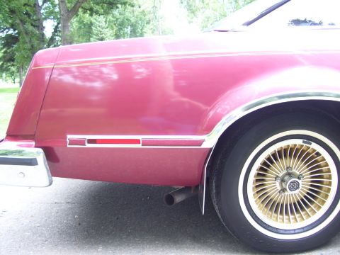 1979 Ford Thunderbird - The rear quarter panel and wheel of a maroon vehicle are visible, chrome trim and gold turbine-style wheels.