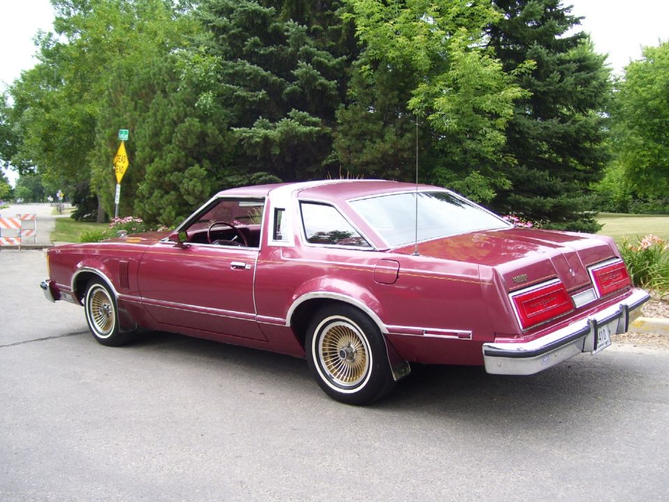 Maroon coupe with gold wheels parked on a street, rear 3/4 view