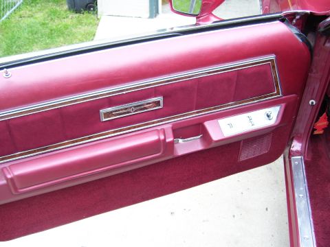 1979 Ford Thunderbird - The interior door panel of a maroon vehicle shows velour upholstery and wood trim details.