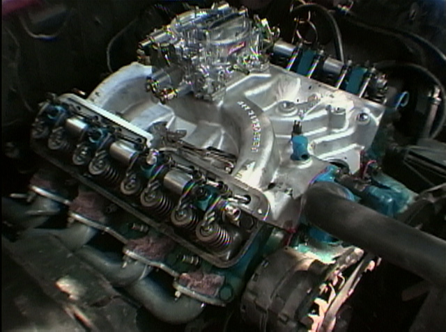 V8 engine with exposed valve springs, silver intake manifold and four-barrel carburetor