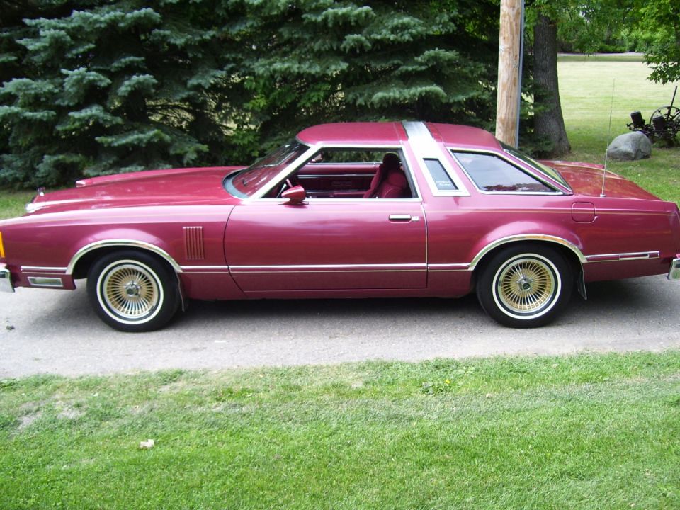 Burgundy 1970s Thunderbird coupe, side view, on gravel driveway