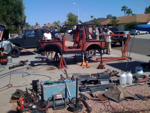 Suzuki Samurai - A red Suzuki Samurai frame and body tub sits stripped down on jack stands in a driveway, surrounded by removed components including axles,…