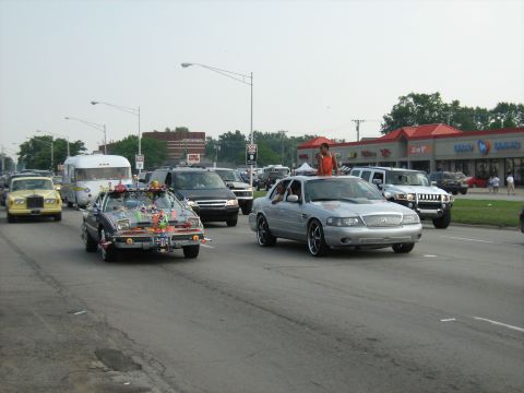 1988 Mercury Grand Marquis - Silver sedan driving in traffic with a person standing on its roof.