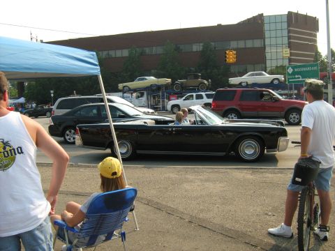1988 Mercury Grand Marquis - A black convertible cruises down the street, carrying passengers, during a car show event.