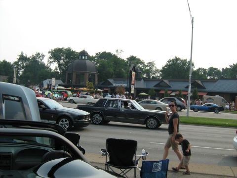 1988 Mercury Grand Marquis - A dark sedan drives past a crowd gathered for an outdoor event.