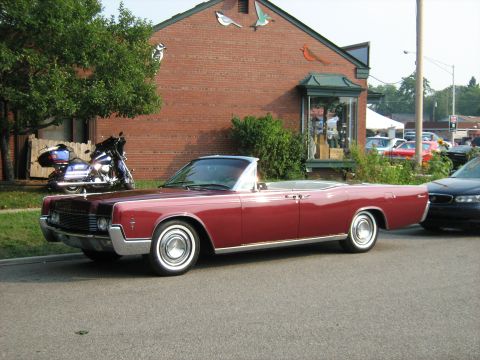 1988 Mercury Grand Marquis - A classic red convertible is parked curbside next to a motorcycle and other vehicles.