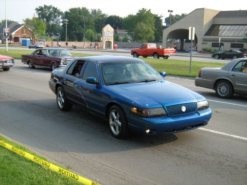 1988 Mercury Grand Marquis - A blue sedan cruises down the road, its modern grille and headlights distinguishing it from older models.